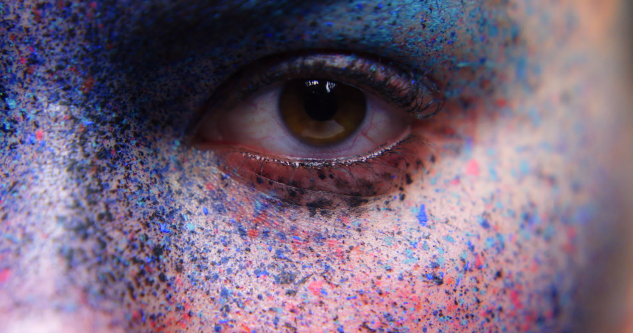Eyes, art and creative with the eye of a woman opening and her face covered in different color paint. Beauty, artistic and eyes with a female in studio with light fading in and out for effect