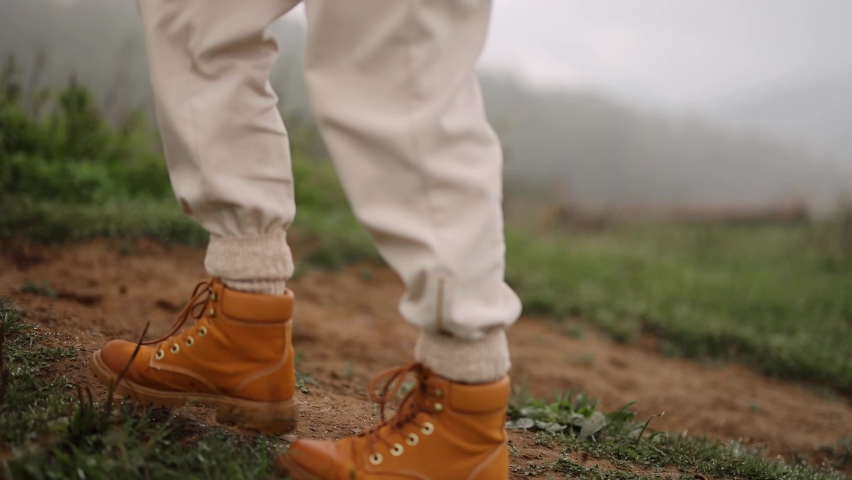 Woman walks with dog on mountain meadow, close-up on boots, side view