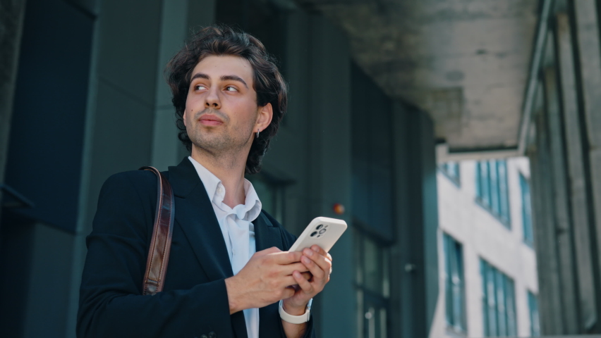 Caucasian businessman is standing near the business centre, answering on the work chats on the social media. Male boss near his work place using smartphone, texting with clients, swiping apps | Shutterstock HD Video #1094982155
