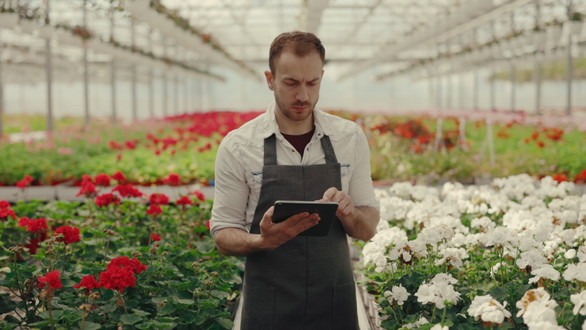 Male garden worker is going in the flower row counting flowers and writes down the information in the digital tablet. People and professions concept | Shutterstock HD Video #1094982183