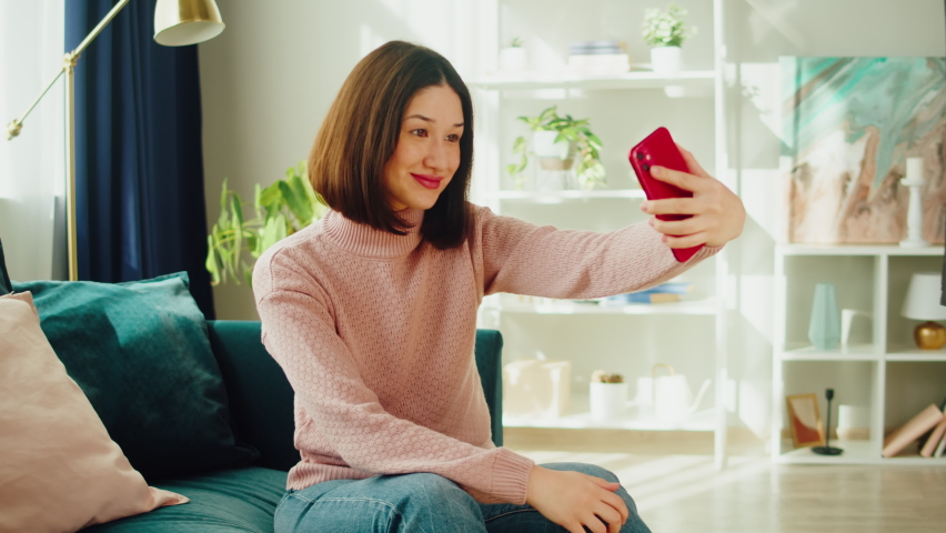 Asian smiling woman talking on video call. Young Korean female student speaking on smartphone, using virtual conference, sitting on sofa in living room. Communicating online via internet. | Shutterstock HD Video #1094982927