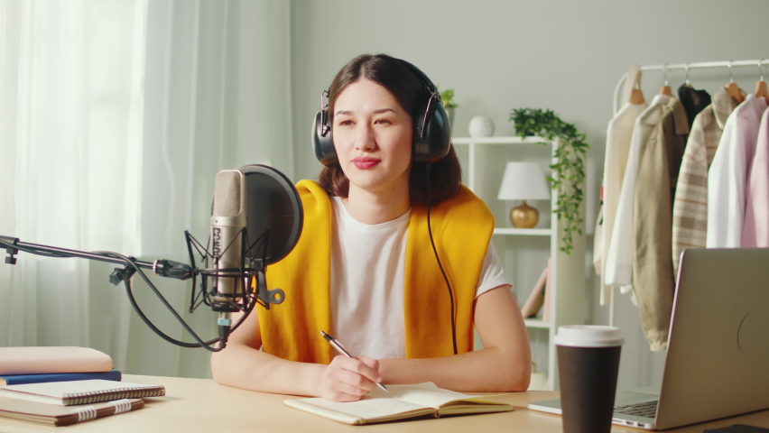 Interview, young woman recording podcast. Podcaster writing notes, Korean female student making audio, using microphone and laptop, broadcasting studio. | Shutterstock HD Video #1094982945
