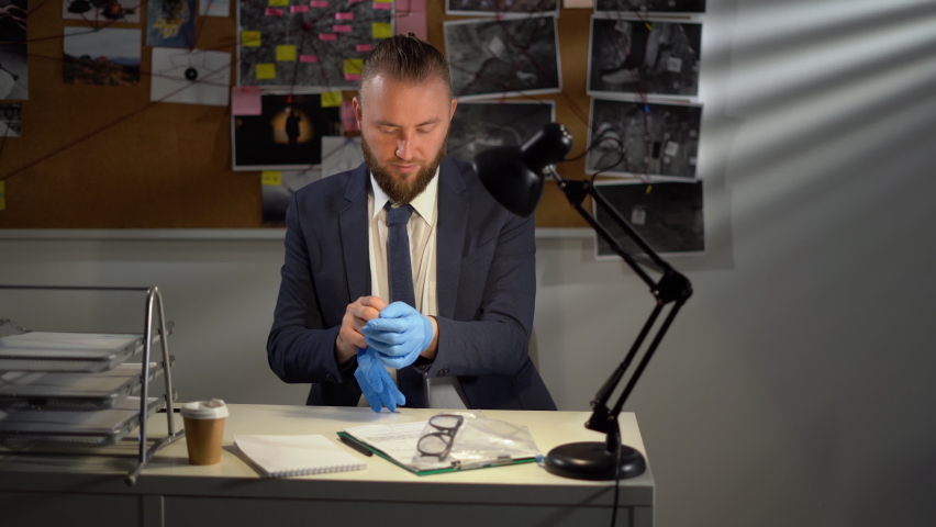 Young serious male detective in uniform on workplace with documents and evidence while learning criminal profiles during investigation | Shutterstock HD Video #1094985249