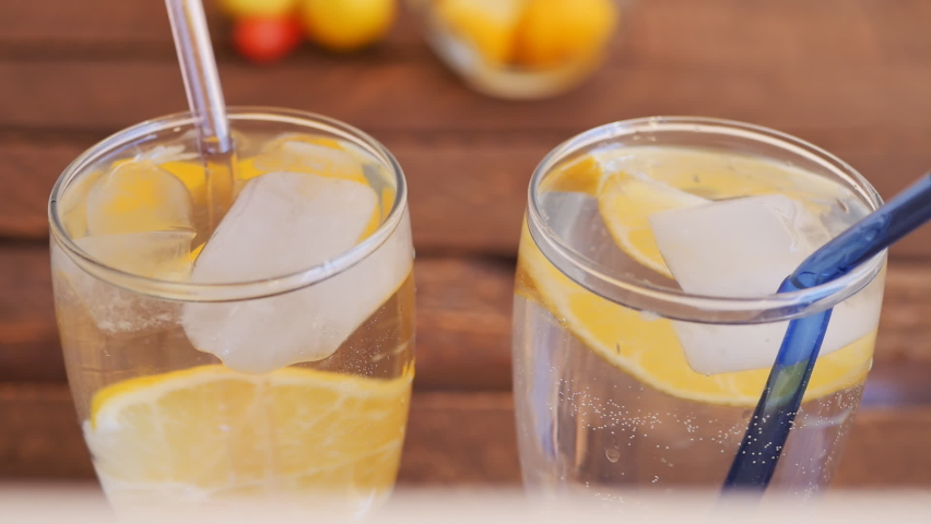 Tall glass glasses with carbonated drink, floating ice cubes, fresh lemon wedges and reusable glass drinking straws inserted. Dolly shot, close up. brown background | Shutterstock HD Video #1094985537