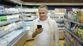A middle-aged man walks through a grocery store talking on a video link. Headphones in the ears. Shopping trip. Modern communication