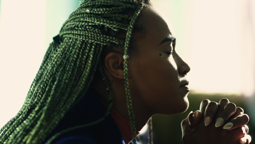 Spiritual African American praying to God. A religious black hispanic latina adult girl in prayer profile closeup face. Person worships to divinity