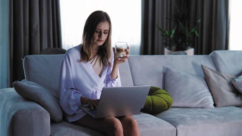 Pretty female freelancer using laptop, working from home and drinking coffee. Woman student studying online remotely, doing research, drinking a tea from a cup | Shutterstock HD Video #1094988725
