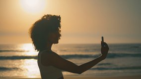 Smiling young woman making selfie at sunrise standing Ursa beach closeup. Cheerful african american girl posing phone camera on beautiful nature. Attractive lady taking photo using smartphone outdoors - Powered by Shutterstock - Get 15% off with code: PIKWIZARD15