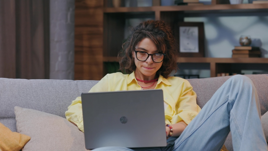 Serious young female freelancer working freelance from home. Works sitting on sofa on laptop, focused girl using computer to study online at home, female user, internet remote work, programming. | Shutterstock HD Video #1094990801