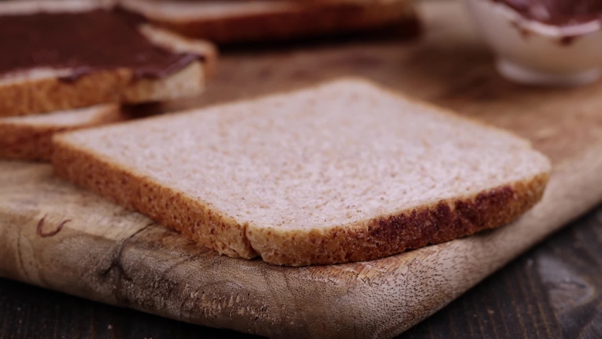 Spread chocolate butter on bread while cooking breakfast, making breakfast from wheat bread with bran and chocolate butter | Shutterstock HD Video #1094990917