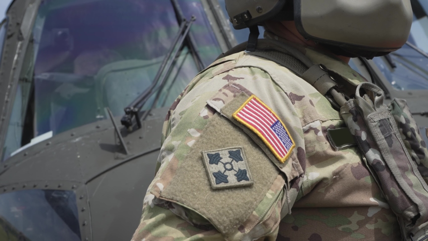American military helicopter pilot soldier with modern helmet set navigate in front of landed chopper.Air force concept