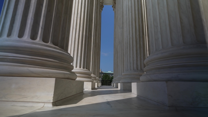 Wide angle pushing through very large towering columns in front of US Supreme Court building in Washington, DC showing judicial power over people and business. Royalty-Free Stock Footage #1094994237