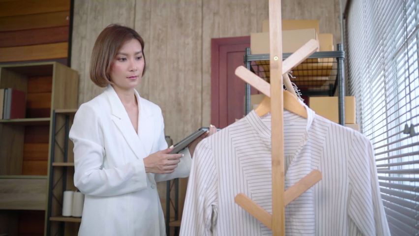 Selective focus Beautiful Asian working woman using tablet checking shipping delivery order on shelves. Successful young female fashion designer have order online from customer. 