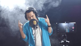 Asian Man With Headphone Singing Into A Condenser Microphone While Recording Video By Smartphone On The Black Background
