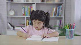 4k video footage little child wearing pink shirt holding pencil or doing homework or wood color painting with colorful paints. Asian girl using wood color drawing color. Baby artist activity lifestyle