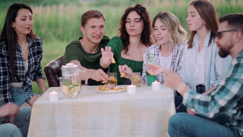 Group of friends are relaxing together outdoor. Young people are sitting at the table, having fun talking and eating food. | Shutterstock HD Video #1095005365