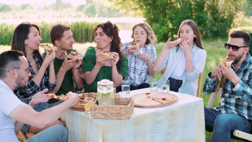 Group of friends are relaxing together outdoor. Young people are sitting at the table, having fun talking and eating pizza. | Shutterstock HD Video #1095005369
