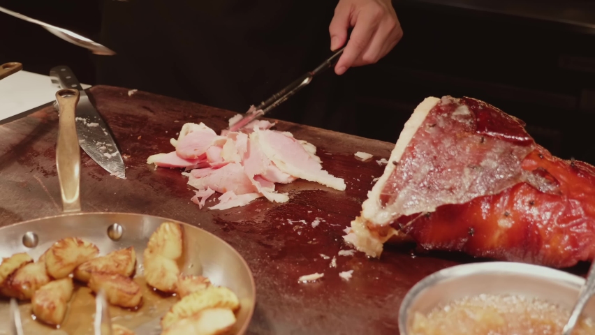 Chef slices roasted pork ham from the smoked leg in luxury restaurant in modern expensive hotel. Concept of celebrating Thanksgiving day or Christmas party | Shutterstock HD Video #1095005531
