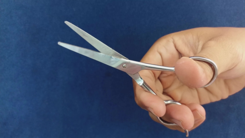Hands holding scissors and practicing using them by opening and closing the scissors. with a blue background | Shutterstock HD Video #1095006057
