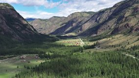 Aerial drone video of of the intermountain valley in Altai near Aktash. The structures of tourist campsites are visible in the meadows. Under the mountain lies the main road of Altai Chuisky Trakt