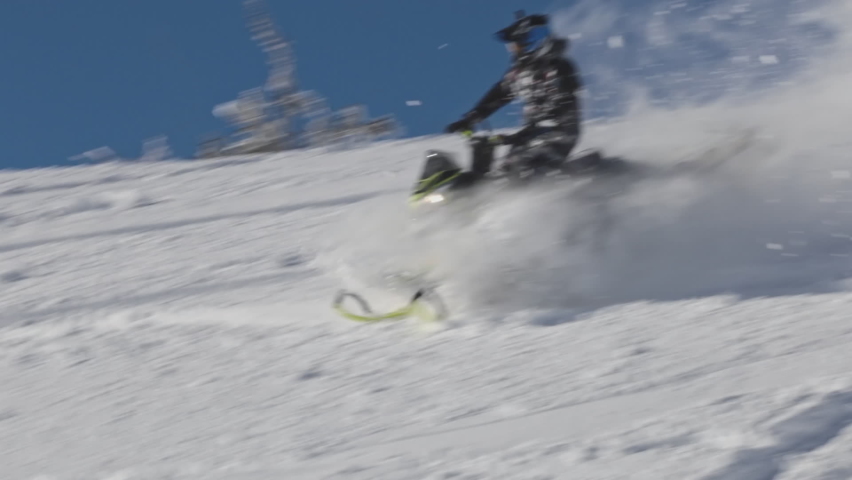 snowmobiler. a professional snowmobile pilot makes extreme jumps against the background of a blue sky with plumes of snow. prores raw
