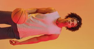 Vertical video of biracial male basketball player with ball on orange background. Sports and competition concept.