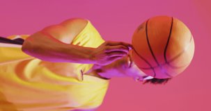 Vertical video of biracial male basketball player spinning ball on pink background. Sports and competition concept.