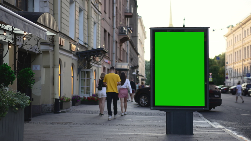 4k Billboard green screen stands and people walk along city street spbd. Mockup poster with advertising standing in open air, pedestrians walking and cars driving along road on summer day. Empty