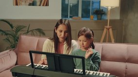 Asian mom and daughter learn to play the piano using a digital tablet.