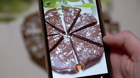 Female Hands Shoots Video of a Chocolate Pie in Kitchen on a Smart Phone. Blogger takes pictures, a photo review of food on a mobile phone camera. Photographing food. Home kitchen. 4K. Close up.