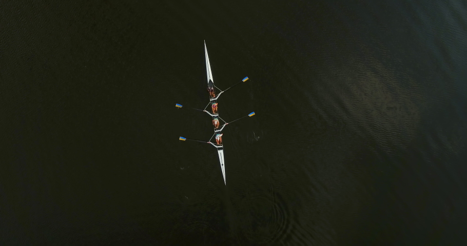 Cinematic top-down drone shot of a sport canoe with a team of four paddling through calm water, aerial view. Athletes training before competition in sports rowing in kayaks Kyiv Ukraine. 