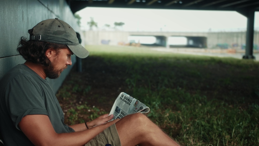 Tired homeless man, refugee tourist on a bench in the park drinking beer or wine, with backpack. Crisis, immigration and unemployment.
