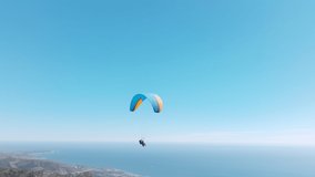 Slow motion up in the air, cinematic aerial drone footage above Malibu USA. Extreme paraglider flying against a clear blue sky, sunbeam shines into camera. Man with instructor flies with paraglide 4k