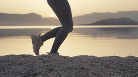 Slow motion video of female legs close up running on the beach at sunrise. A girl on a morning jog by the ocean is running around in sneakers. High quality 4k footage