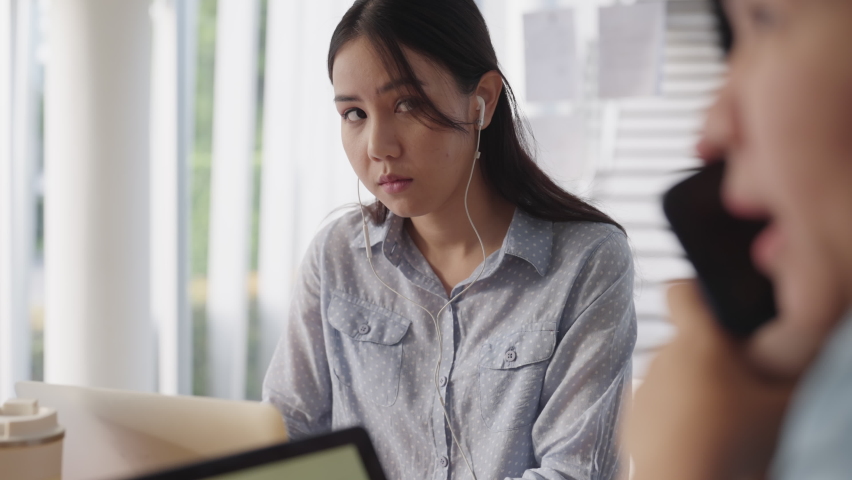 Young adult asia Gen Z female rolling eyes frown face to noisy rude shame worker in hybrid office toxic people loud noise. Moody bored woman stress work social issue angry upset annoy in boring job. | Shutterstock HD Video #1095049249
