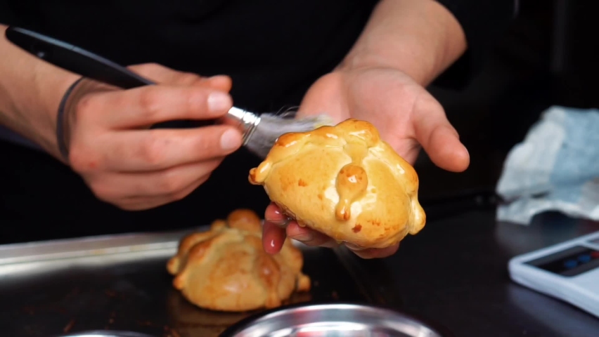 Horizontal video of an unrecognizable man putting egg and sugar to a pan de muerto in a kitchen. Royalty-Free Stock Footage #1095049939