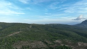 Prores footage of drone flying over green mountains of Trucafort with eolic park in background. Pradell de La Teixeta, Tarragona in Spain. Aerial forward. Sky for copy space