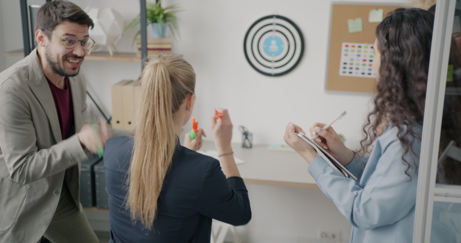 Excited businesswoman is playing darts in workplace relaxing laughing with carefree colleagues. Modern business and youth lifestyle concept. Royalty-Free Stock Footage #1095054213