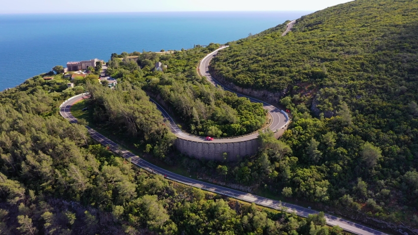 Red car speeding on a winding mountain road in sunny, Portugal - Aerial view
