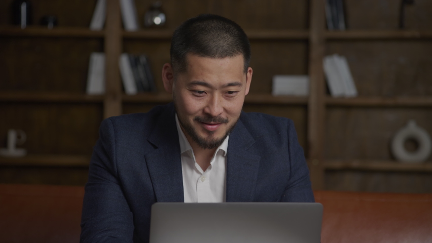 Asian businessman working hapy on his laptop computer in his loft office wearing a suit