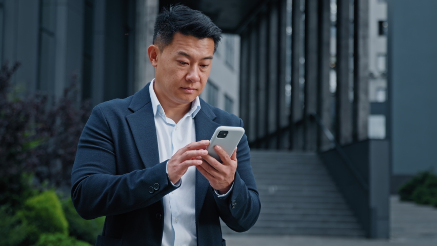 Asian businessman in city has mobile problem with telephone. Middle-aged CEO employer entrepreneur outdoors browsing phone feeling upset with broken mistake error online cellular bad connection lost Royalty-Free Stock Footage #1095073035