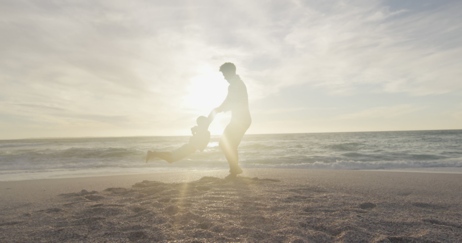 Animation of christmas text over biracial man and his son at beach. Christmas, tradition and celebration concept digitally generated video.