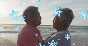 Animation of snow falling over senior biracial couple at beach. Christmas, tradition and celebration concept digitally generated video.