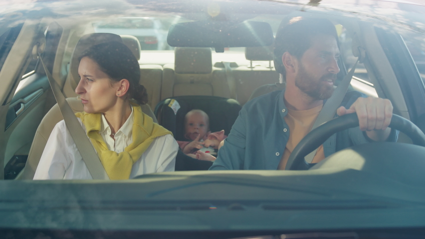 Front view of couple of young woman and man sitting in car, talking to each other s, gesturing. Baby boy sitting in baby car seat. Problem, stress. Fasten seat belt, toddler Royalty-Free Stock Footage #1095078131