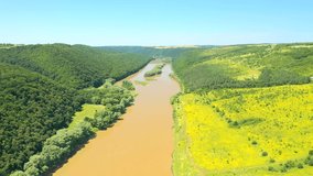 A large river flows through splendid fields and green forests. Footage from a bird's eye view. Location place Dniester canyon, Ukraine, Europe. Cinematic shot. Filmed UHD 4k video. Beauty of earth.