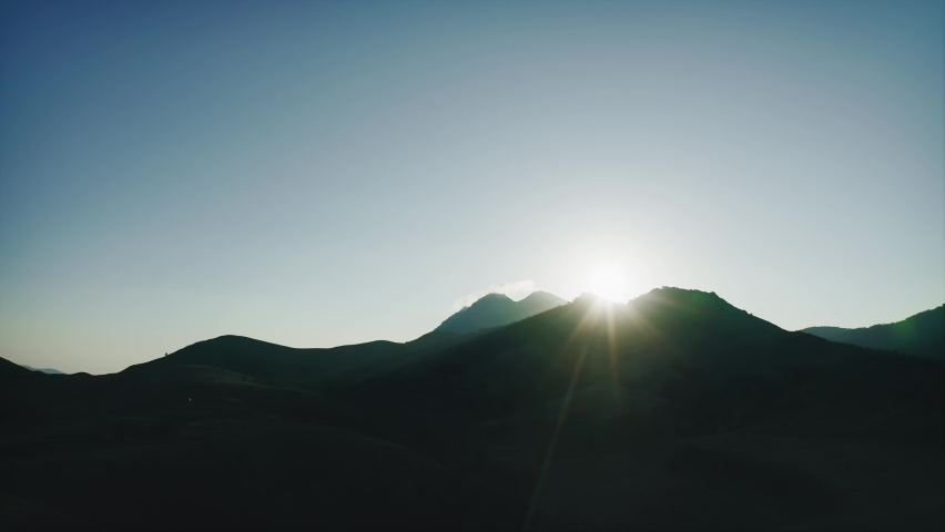 Setting sun over black silhouette of mountain. Drone aerial shot.
