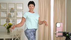 Mature woman recording trendy dance moves for social media account at home. Woman 50-60 years old shooting short video on smartphone. Concept social media, stories, and trendy dance.