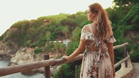 Portrait beautiful young woman tourist enjoys top view. Summer sunset nature, sky rocks coast sea water waves. Happy girl fashion model travel in Spain. Costa Brava beach. Spring clothes long dress