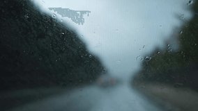Glass rain auto. A car ride in a heavy downpour. Blurry traffic on the road, headlights of oncoming cars out of focus. The concept of bad weather, storm, hurricane. A gray, rainy, dreary autumn day.