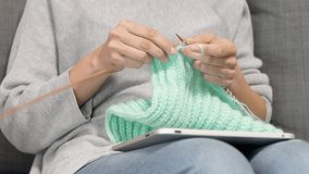 Woman holding digital tablet computer on her lap, looking at screen and knitting sweater. Woman learning knitting, watching video tutorial, online class lesson, follow knitting patterns
